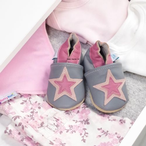 Graue und rosa Lederschuhe in einer Schublade mit Babykleidung.