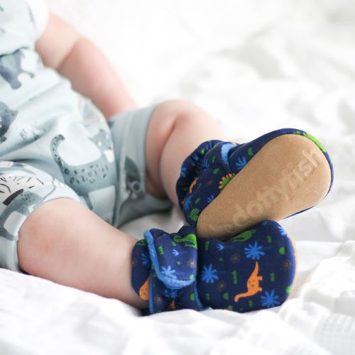 Babyjunge trägt dunkelblaue Dotty Fish Babystiefel aus Baumwolle mit blauem Fleecefutter und buntem Dinosauriermuster.