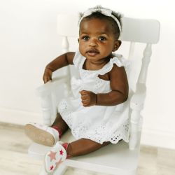 Kleinkind mit weißem Leder Dotty Fish erste walker barfuß Schuhe mit rosa Sternen, sitzt auf Stuhl.