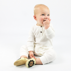 Baby trägt cremefarbene Dotty Fish Schuhe mit Löwenmotiv und weißem Babywuchs, sitzt auf dem Boden.