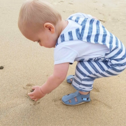  Kleiner Junge spielt am Strand und trägt graue Dotty Fish Barfußsandalen aus Leder.