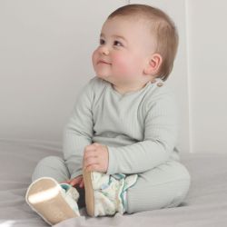 Baby-Junge sitzt und trägt cremefarbene Dotty Fish-Schuhe aus Baumwolle mit dunkelgrünem Fleece-Futter und Dschungeltiermuster.