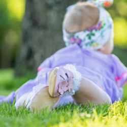  Kleinkind-Mädchen im Gras liegend mit rosa Leder Dotty Fish ersten Walker barfuß Sandalen mit rosa Blumen.