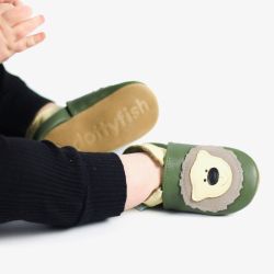 Kleiner Junge sitzt auf dem Boden und trägt grüne Krabbelschuhe von Dotty Fish mit cremefarbenem Bärendesign.