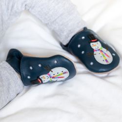 Sitzender Junge mit navyfarbenen Dotty Fish Barfußschuhen und weißem Schneemann mit schwarzer Mütze und gesticktem Regenbogenschal.