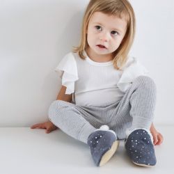 Mädchen im Kleinkindalter, sitzend, trägt dunkelgraue Dotty Fish Kinderhausschuhe aus Wildleder mit silbernen Sternen.